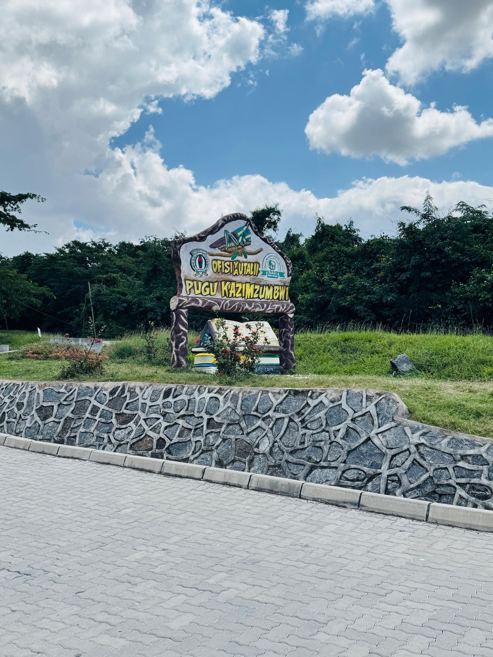 Tourism office entrance sign at Pugu Kazimzumbwi, framed by a stone wall and blue sky